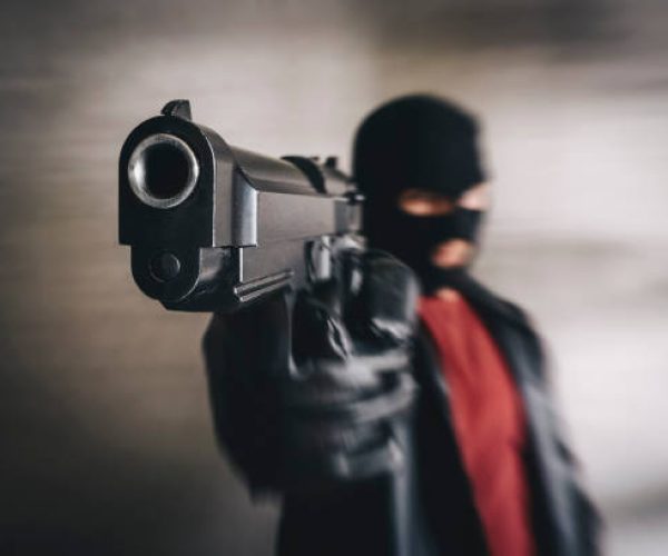 shooter in black mask attacks. Armed terrorist, thief with pistol in hands. criminal targeting with gun. Mafia gangster point gun in camera. Focus on pistol barrel. concept of banditry theft crime