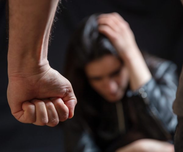 Woman abuse, Young woman scared holding head with hands, male clenched fist close up. Domestic violence, husband against wife. Dark room background