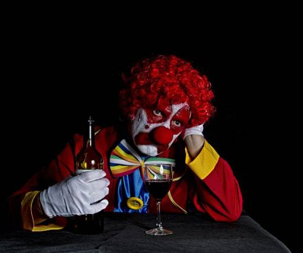 clown with sad face leaning on table drinking