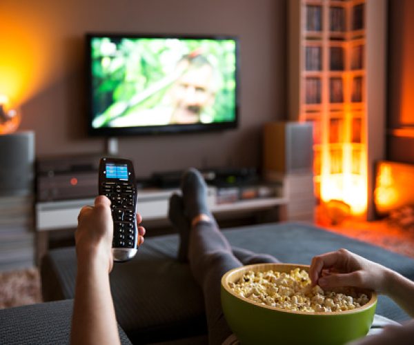 Woman relaxing at home watching tv and eating popcorn