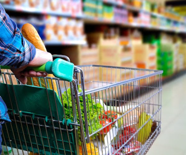 Man pushing shopping cart full of food in the supermarket aisle. Elevated rear view. horizontal composition